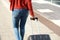 Behind of young black woman walking and pulling suitcase