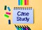 On a beige background, a notebook with the words CASE STUDY, bright felt-tip pens and stickers