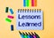 On a beige background, a notebook with the words LESSONS LEARNED, bright felt-tip pens and stickers