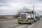 Beige and brown classic big rig semi truck with chrome accessories and oversize load sign transporting cargo on flat bed semi