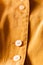 Beige button on a mustard orange blouse, vertical photo