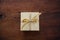 Beige closed gift box with gold color ribbon on wooden table background