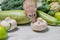 A beige decorative dumbo rat sits on vegetables. A cute mouse sniffs a white mushroom.