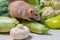 A beige decorative dumbo rat sits on vegetables. A cute mouse sniffs a white mushroom.