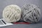 Beige and gray skeins of thick cord for crocheting. The red hook lies in front of the skeins