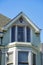 Beige house facade with white accent paint near roof and brown tiles with double gable design and blue sky background