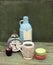 Beige knitted mug, macaroons, blue bottle and rough paper bag background on green grunge background. Nude still life.