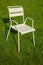 A beige metal chair stands on the lawn. Long hard shadows on the green grass. Urban theme. Theme of loneliness