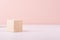 Beige natural wood podium of cube shape on white wood table and pastel pink wall. Showcase for cosmetic products, packings.