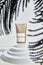 Beige plastic tube, face, body cream on white podium with palm leaves.
