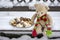 Beige plushy teddy bear with red green striped knitted scarf sitting with Christmas cookies on the bench covered with white snow