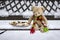 Beige plushy teddy bear with red green striped knitted scarf sitting with Christmas cookies on the bench covered with white snow