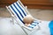 Beige shells of various sizes lie on a little vintage decoration striped beach chair with a blue sea, side view