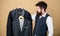 Being a tailor. Mens tailor. Hipster holding tailor made coats at department store. Bearded man choosing suit jacket in