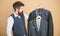 Being a tailor. Mens tailor. Hipster holding tailor made coats at department store. Bearded man choosing suit jacket in