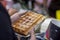 Belgian fresh warm waffle with powdered sugar in hands of buyer. Gastronomic dainty products on market counter, real