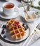 Belgian waffles with blueberries and red currants, honey and tea on a white table