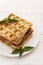 Belgian waffles with fresh mint on a white plate on a white tablecloth, retro toning, close-up