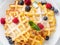 Belgian waffles with raspberries, blueberries, curd, close-up, top view. Healthy homemade breakfast, light concrete background