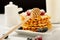 Belgian waffles with raspberries and sieving sugar powder and honey served with jug of milk on a white table