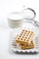 Belgium wafers with sugar powder on ceramic plate and strainer on white table