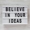 `Believe in your ideas` words on a lightbox over white wooden background, top view. Flat lay, from above, overhead