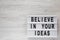 `Believe in your ideas` words on lightbox over white wooden surface. Flat lay, from above, overhead. Space for text