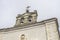 Bell tower of a church with a cross and weather vane above and details carved in stone on the facade