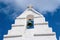 Bell tower with cross in Mykonos, Greece. Chapel building detail architecture. White church on cloudy blue sky. Religion