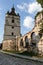 Bell tower, part of the wall and a forged iron gate on the background of the blue sky.