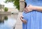 Belly of pregnant woman in a blue dress close-up on the river Bank in the city, hands hugging her stomach, yellow manicure