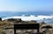 Bench in a cliff. Wild sea with big waves, foam and mist. Sunny day, Galicia, Spain.