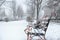 Bench covered with fresh snow on storm day in city park.