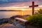 a bench and a cross on a rocky shore with a sunset