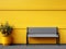 a bench next to a potted plant in front of a yellow wall