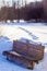 The bench in the park among the snowy banks is illuminated by the rays of the setting March sun. Behind the footprints in the snow