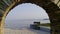 Bench by shore seen through arch