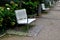 Benches with metallic shiny stainless steel construction, armrests, white wood paneling in public parks. under a bench of granite