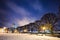 Benches under snow along walkway, trees and street lights on embankment. Winter cityscape at twilight. St. Petersburg, Russia.