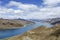 Beneath a plethora of puffy, white clouds, Lake Yamdrok glows turquoise between the desert mounatains of the Tibetan Plateau