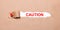 Beneath the torn strip of kraft paper attached with a red button is a white paper labeled CAUTION