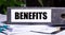 BENEFITS is written on a gray file folder next to documents. Business concept