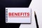 BENEFITS written in red on a black and white background near the pen