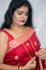 A Bengali girl wearing the red sari and golden ornaments giving poses in front of a white curtain