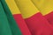 Benin flag with big folds waving close up under the studio light indoors. The official symbols and colors in banner