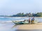 BENTOTA, SRI LANKA - NOVEMBER 14, 2019: Fishermen sort through nets next to a wooden boat on the Indian ocean shore on the island