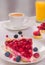Berry cake on a plate multiple fresh berries on table glass of orange juice and white cup of coffee