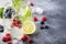 Berry and citrus soft drinks and cocktails in glass bottles on gray stone table background, copy space