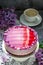 A berry mousse cake with chocolate base and juice jelly, decorated with lilac flowers, served with coffee.