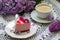 A berry mousse cake with chocolate base and juice jelly, decorated with lilac flowers, served with coffee